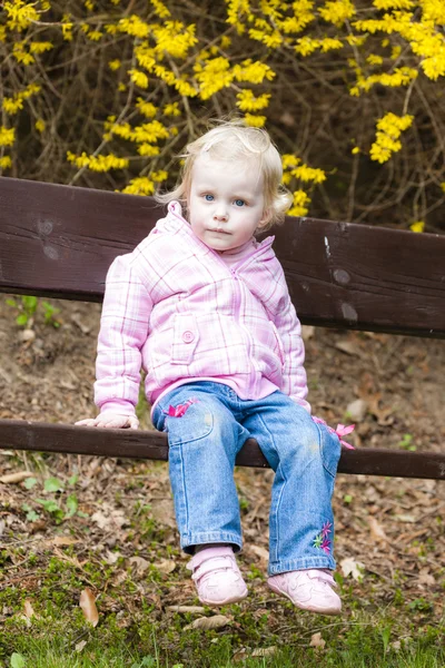 Petite fille assise sur un banc au printemps — Photo