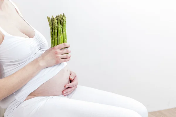 Close up of pregnant woman holding green asparagus — Stock Photo, Image