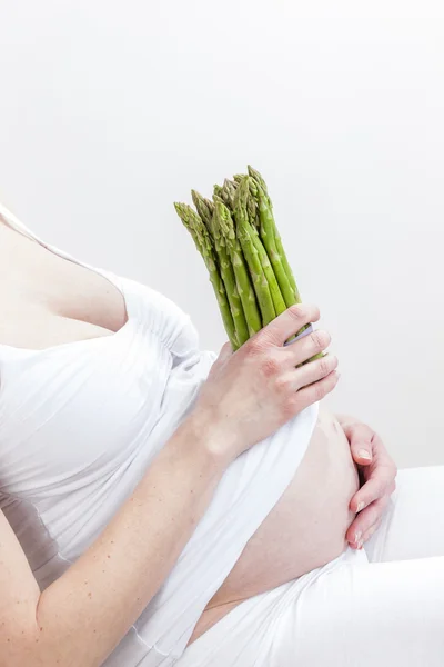 Närbild på gravid kvinna med grön sparris — Stockfoto