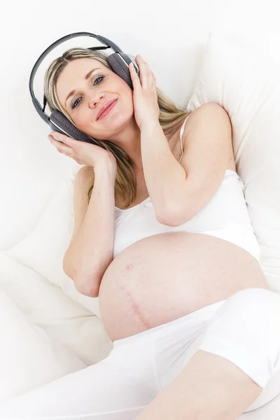 Těhotná žena se sluchátky odpočívá v posteli — Stock fotografie