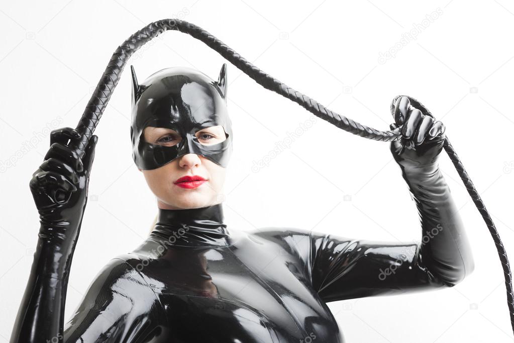 Standing woman wearing latex clothes with a whip