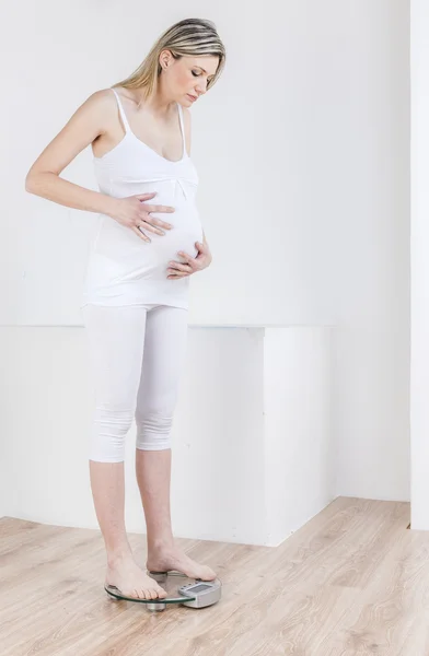 Беременная женщина стоящая на весах — стоковое фото