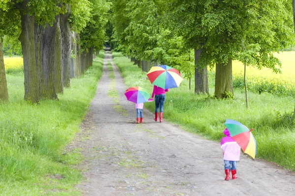 Mother and her daughters with umbrellas in spring alley — Stock Photo, Image