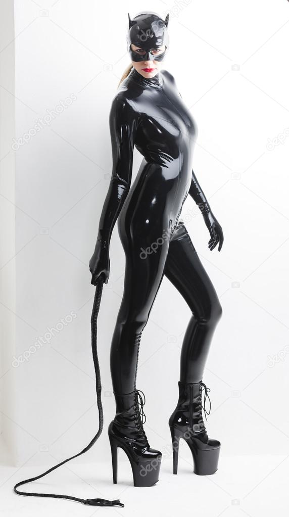 standing woman wearing latex clothes with a whip
