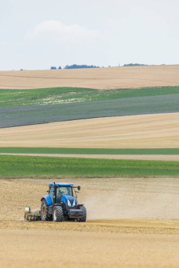 Mavi traktör temiz bir gökyüzünün altında kırsal alanda kuru toprak yetiştiriyor.