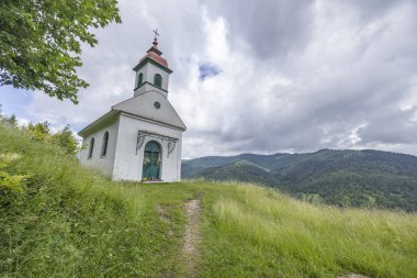 Dağlara tepeden bakan ve bulutlu gökyüzüne bakan bir tepede duran beyaz şapel.