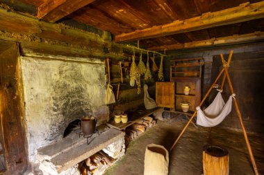 İçinde şömine, kurutulmuş otlar, çömlek ve bebek beşiği olan eski ahşap bir ev.