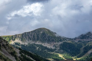 Ormanları olan dağlar ve bulutlu bir gökyüzünün altında vadiden geçen bir yol.