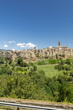 Pitigliano, bir ortaçağ kasabası, açık mavi gökyüzünün altında yeşil yapraklı bir uçurumda duruyor.