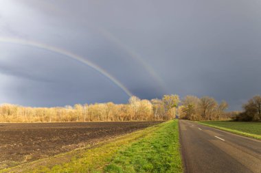 Bir yola, ağaçlara ve çarpıcı bir gökyüzünün altında yeni sürülmüş tarlalara iki kat gökkuşağı yayılıyor.