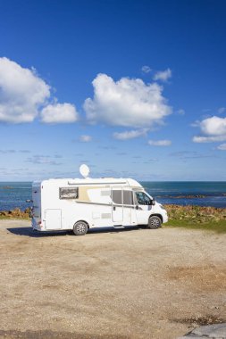 Güneşli bir günde, beyaz eğlence aracı deniz kenarındaki pis bir arazide park halindedir.