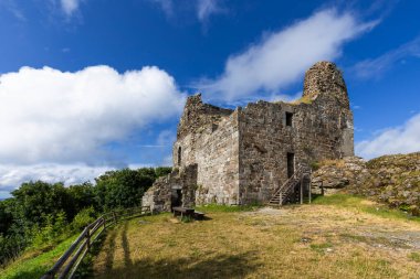 Antik şato harabeleri beyaz bulutlu, parlak mavi bir gökyüzünün altında duruyor.