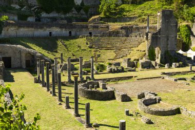 Roma tiyatrosu Volterra, İtalya 'da güneşli gökyüzü altında katmanlı oturma yerleri ve sütunları olan harabeler