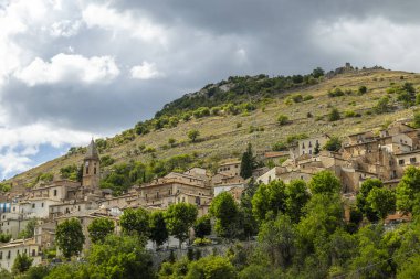 İtalya 'nın Abruzzo kentindeki bulutlu gökyüzünün altında tepe yamacına tutunan Calascio köyü evleri