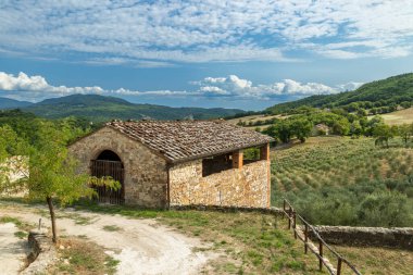 Geleneksel taş bina bir tepenin üzerinde duruyor, İtalya 'da zeytin ağaçları ve yeşil tepelere bakıyor.