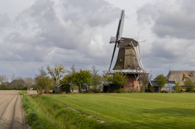 Yeşil bir tarlada duran yel değirmeni Peazens 'te bulutlu bir gökyüzünün altında tarlaya yakın.