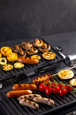 Çiğ ve pişmiş et ve taze sebzeler modern elektrikli ızgarada pişiyor.