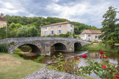 Tarihi taş kemer köprüsü Cole Nehri 'ni geleneksel evler ve ötesinde yeşil ağaçlarla geçer.