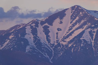 Dağ zirvesi kısmen karla kaplı, günbatımının ya da gündoğumunun yumuşak ışığını yansıtıyor