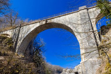 Fransa 'nın Doubs şehrinde açık mavi gökyüzüne karşı geniş kemerli taş köprü