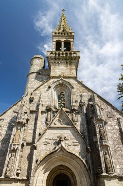 Karmaşık heykeller ve mavi gökyüzünün altında yüksek bir kule bulunan tarihi taş kilise.
