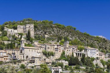 Açık mavi gökyüzüne karşı dik bir yamaca tutunan tarihi köy binaları