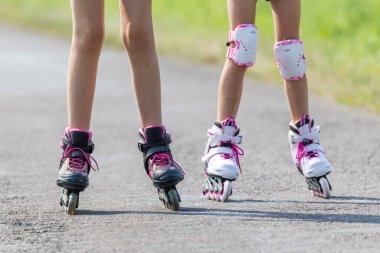 Genç kızlar yaz boyunca asfalt bir yolda açık havada paten kaymaktan zevk alıyorlar.