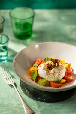 Kremalı burrata peyniri olgun vişneli domates ve taze fesleğen yapraklarıyla servis ediliyor.
