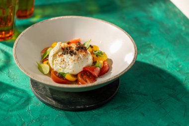 Renkli domatesler ve yeşil bir masada fesleğen yapraklarıyla servis edilen taze burrata peyniri.