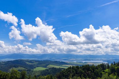 Geniş manzara yeşil kayan tepeleri, derin mavi suyu ve mavi gökyüzünün altındaki uzak dağları gösteriyor.