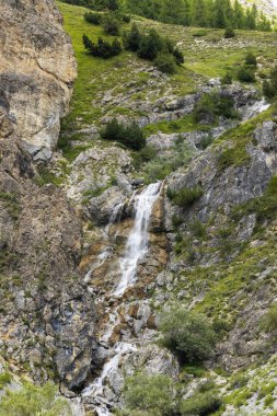 Arjanterya, Piedmont, İtalya 'daki dağlarda kayaların ve yeşil bitkilerin üzerinden güçlü bir şekilde akan şelale.
