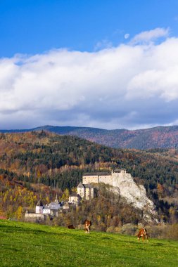 Orava Kalesi, mavi gökyüzünün altında otlayan ineklerle dolu bir sonbahar dağ manzarasına yerleşmiş.