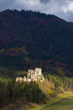 Likavka Kalesi bir orman tepesinde harabe, arka planda sonbahar ağaçları bulutlu gökyüzünün altında