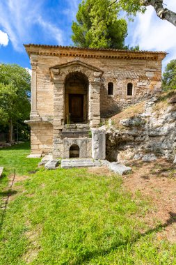 Sütunlar ve yeşil çimen ve ağaçlarla kaplı kadim taş tapınak binası.