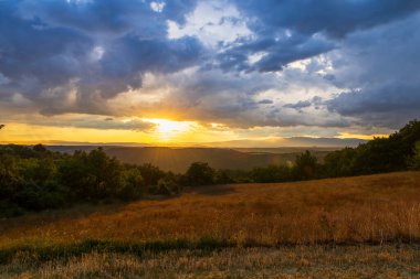 Fırtınalı bulutların ardında batan güneş, Entrevennes, Fransa 'nın tepelerine ve tarlalarına altın ışık saçıyor.