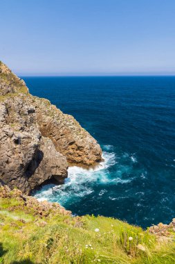 Cantabria 'da güneşli bir günde kayalık kayalıklarla buluşan derin mavi deniz suyu