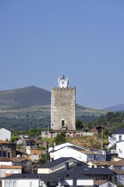İspanyol kasabasındaki geleneksel evlere bakan bir tepede saati olan tarihi taş kule.