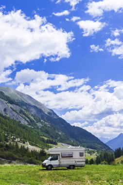 Kampervan yeşil dağ yamacına park etmiş, doğada özgürlüğün ve maceranın tadını çıkarıyor.