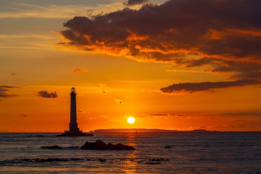 La Hague, Normandiya 'da canlı bir günbatımı sırasında kayalık sularda duran deniz feneri