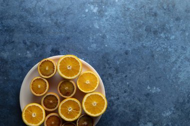 Dilimlenmiş taze portakallar bej bir plaka üzerinde mavi bir arkaplanda canlı renkler sunar.