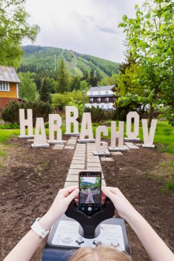 Harrachov kasabası tabelası ve dağları cep telefonu kullanarak gezen bir turist.