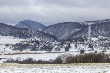 Önünde beyaz bir tarla olan tepeler ve ormanların arasında yuva yapmış bir köy.
