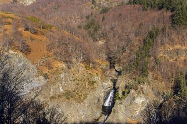 Fransa 'nın Pereyres kentinde sonbahar ağaçlarıyla çevrili kayalık bir vadide çağlayan şelale.
