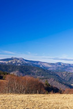 Açık mavi gökyüzü ve tepeleri kaplayan kış bitkileriyle Ardeche dağlarının geniş manzarası