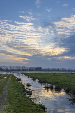 Sougeal, Fransa 'da kırsal alan, sakin bir dereyle renkli bir günbatımı gökyüzünü yansıtıyor.