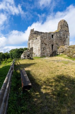 Yeşil çimenler ve mavi gökyüzü olan bir tepede duran tarihi bir şatonun taş duvarları.