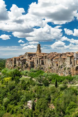 Eski binaların ve mavi gökyüzünün altında bulutlu bir çan kulesinin bulunduğu Pitigliano eski kasabası.