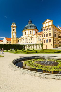 Resmi bahçelerin üzerinde yükselen barok şato mimarisi ve güneşli bir günde dingin bir çeşme.