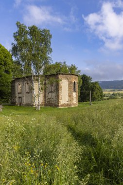Eski kilise harabeleri mavi gökyüzünün altında canlı yeşil bir çayırda duruyor.