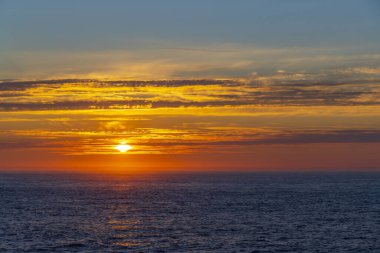 Ufukta altın saat güneşi batıyor, denizin üzerindeki sıcak renklerle gökyüzünü boyuyor.